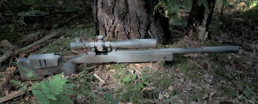 Hand-painted M40A3 airsoft sniper rifle with scope, resting against a tree in the woods